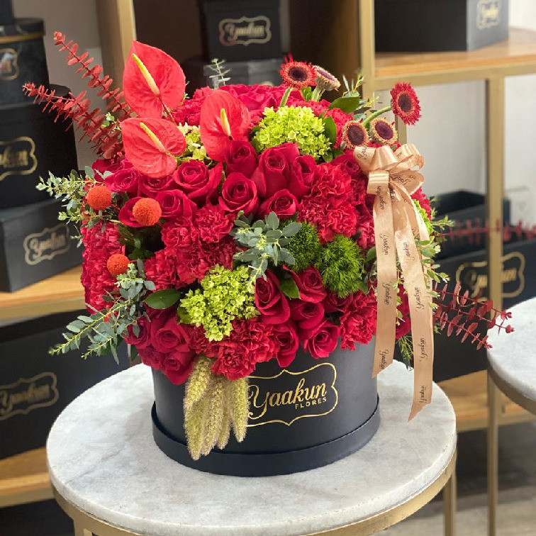 Caja circular negra con 100 rosas y follajes en tonos rojos